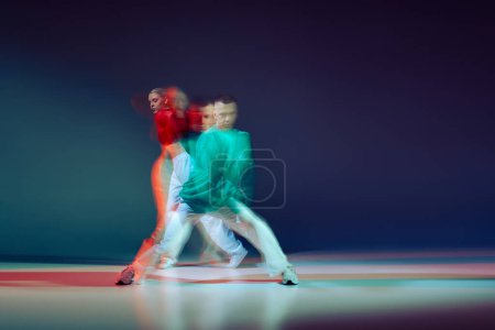 Portrait of young man and woman dancing isolated over dark blue background with mixed lights. Cooperation. Concept of movement, youth culture, active lifestyle, action, street dance, ad