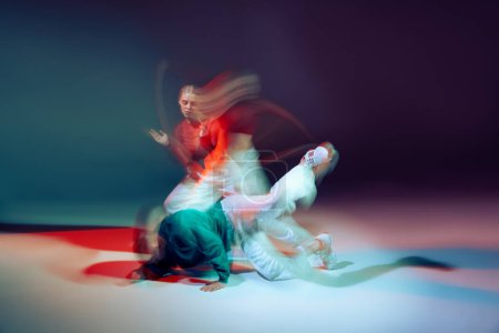 Portrait of young man and woman dancing isolated over green purple background with mixed lights. Contemp performance. Concept of movement, youth culture, active lifestyle, action, street dance, ad