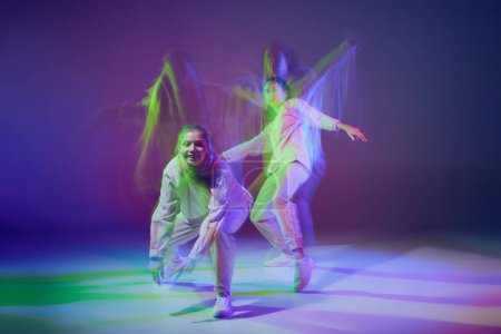 Foto de Retrato de chicas jóvenes bailando hip-hop aisladas sobre fondo azul púrpura degradado en neón con luz mixta. Concepto de movimiento, cultura juvenil, estilo de vida activo, acción, danza callejera, hobby - Imagen libre de derechos