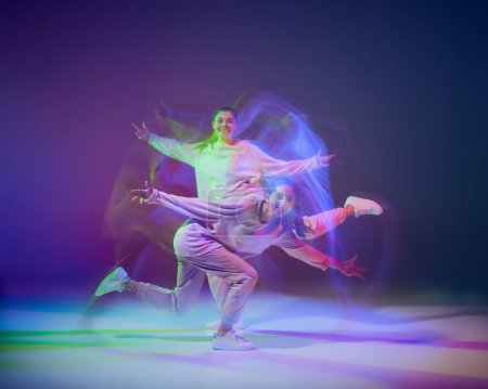 Foto de Retrato de chicas jóvenes bailando hip-hop aisladas sobre fondo azul púrpura degradado en neón con luz mixta. Actuación. Concepto de movimiento, cultura juvenil, estilo de vida activo, acción, danza callejera - Imagen libre de derechos