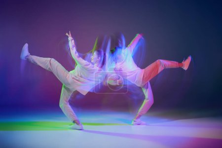 Foto de Dos chicas jóvenes bailando hip-hop aisladas sobre gradiente azul púrpura fondo en neón con luz mixta. Bien coordinado. Concepto de movimiento, cultura juvenil, estilo de vida activo, acción, danza callejera - Imagen libre de derechos