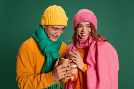Photo for Portrait of young man and woman in bright knitted hat and scarf posing isolated over green background. Happiness and merry. Concept of emotions, winter holidays, fashion, lifestyle, relationship - Royalty Free Image