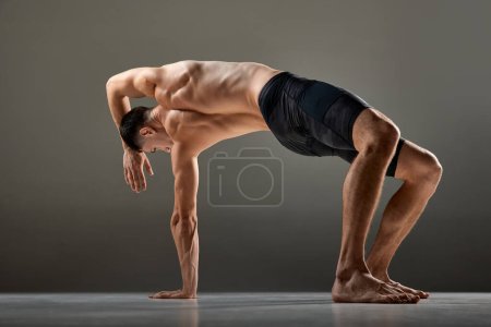 Téléchargez les photos : Portrait d'un athlète masculin flexible montrant des éléments de sport de flux animal isolés sur fond gris. Yoga, fitness, sports à la mode, beauté du corps. Grâce et flexibilité du corps humain - en image libre de droit