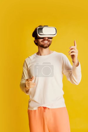 Photo for Virtual world. Studio footage of young Caucasian man wearing casual style clothes using VR glasses isolated over yellow background. Emotions, games, technology, ad - Royalty Free Image
