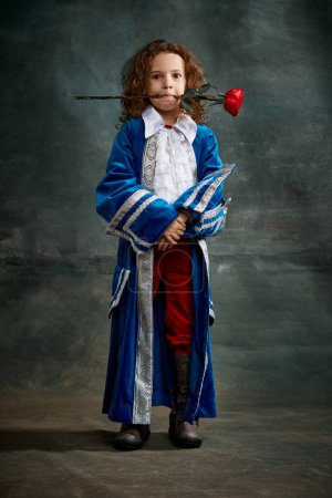 Photo for Emotional kid, little girl wearing costume of prince, musketeer and royal person posing over dark vintage style background. Fashion, theater, beauty, emotions concept. Eras comparison - Royalty Free Image