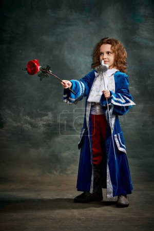 Photo for Emotional kid, little girl wearing costume of prince, musketeer and royal person posing over dark vintage style background. Fashion, theater, beauty, emotions concept. Eras comparison - Royalty Free Image