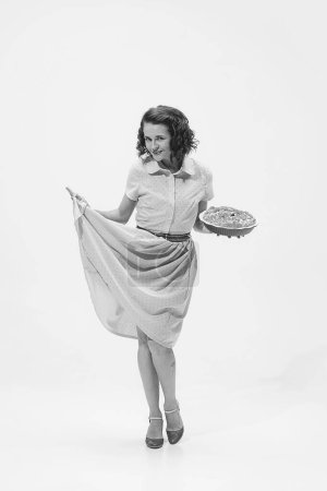 Téléchargez les photos : Portrait de belle femme rétro en robe vintage de style mode tenant tarte aux pommes. Plan noir et blanc. Concept de beauté, style rétro, mode, élégance, années 60, 70, famille. Espace de copie pour la publicité - en image libre de droit