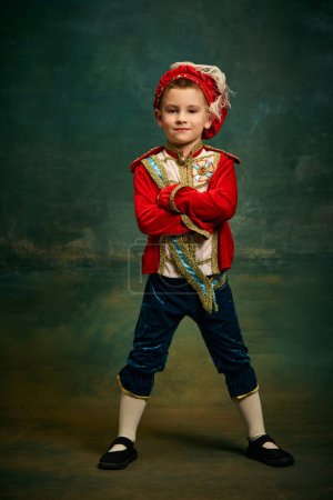 Photo for Portrait of cute little boy dressed up as medieval character, little prince and pageboy posing over dark vintage style background, Fashion, emotions, theater art concept. Eras comparison - Royalty Free Image