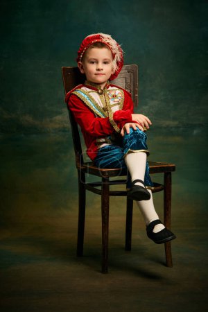 Photo for Portrait of cute little boy dressed up as medieval character, little prince and pageboy posing over dark vintage style background, Fashion, emotions, theater art concept. Eras comparison - Royalty Free Image