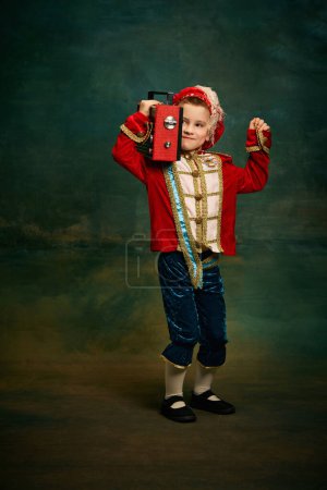Photo for One cute little boy dressed up as medieval little prince and pageboy having fun over dark vintage style background. Vintage fashion, emotions, theater art concept. Eras comparison - Royalty Free Image
