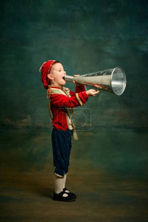 Photo for Attention, breaking news. Little preschool age boy dressed up as medieval little prince and pageboy shouting at megaphone over dark vintage style background. Vintage fashion, emotions concept - Royalty Free Image