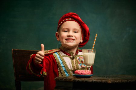 Photo for Nice sign. Little charming kid in historical costume smiling and thumb up over dark green background. Concept of fast food, comparison of eras, retro, vintage, emotions. Looks happy - Royalty Free Image