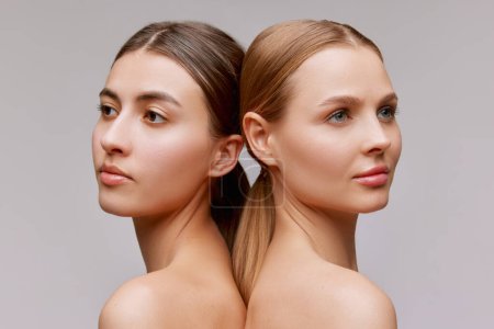 Feelings. Closeup portrait of two adorable young girls with well-kept skin posing over grey background. Couple of models with bare shoulders. Concept of beauty, spa, skin care and health