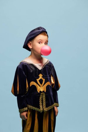 Photo for Surprise. Little charming boy in costume of medieval pageboy, little prince with bubble gum over light blue background. Concept of children emotions, eras comparison, fashion, theater, art, festival - Royalty Free Image