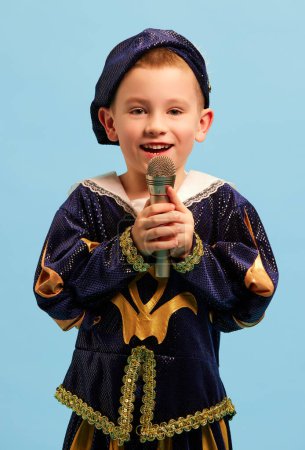 Photo for Happy preschool age boy in costume of medieval pageboy, little prince singing at microphone over light blue background. Concept of children emotions, eras comparison, fashion, music, art, festival - Royalty Free Image