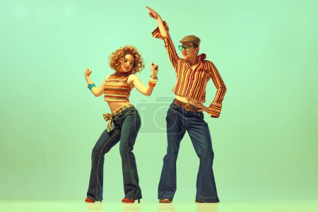 Fröhliche und aktive Tänzer. Zwei aufgeregte Menschen, Mann und Frau in Retro-Klamotten, tanzen Disco vor grünem Hintergrund. 70er, 80er Jahre Mode, Musik, Hippie-Lifestyle
