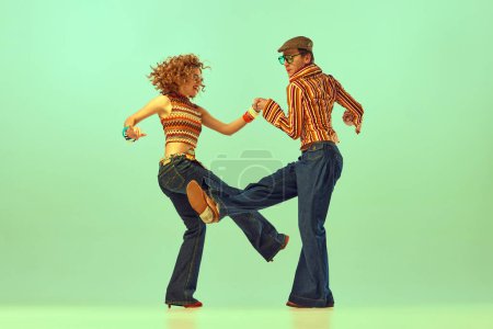 Glück und Spaß. Zwei aufgeregte Menschen, Mann und Frau in Retro-Klamotten, tanzen Disco vor grünem Hintergrund. 70er, 80er Jahre Mode, Musik, Hippie-Lifestyle
