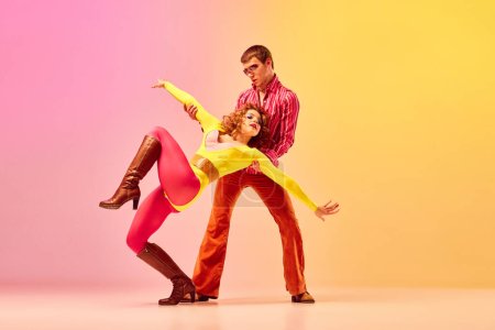 Emotionen in Bewegungen. Junge stilvolle emotionale Männer und Frauen, professionelle Tänzer in Retro-Klamotten tanzen Disco-Tanz über rosa-gelbem Hintergrund. 1970er, 1980er Mode, Musikkonzept