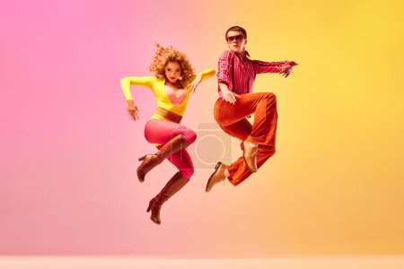Photo for Jumping in new day. Stylish expressive excited couple of professional dancers in retro style clothes jumping, flying over pink-yellow background. Concept of 70s, 80s fashion style, music and emotions - Royalty Free Image