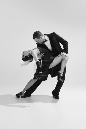 Portrait of stunning couple wearing vintage style clothes and dancing tango over white background. Concept of love and music, temptation and fashion, rich people party concept, american culture, ad