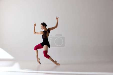 Beauty of contemporary dance. One young ballerina wearing pointe shoes dancing on fingertips over white background.The art, artist, movement, action and motion concept.
