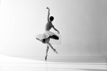 Czarno-białe zdjęcie. Młoda, pełna wdzięku balerina pozująca w studio i demonstrująca elegancki ruch. Sztuka, ruch, działanie, elastyczność, koncepcja inspiracji