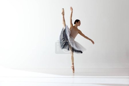 Demonstrate flexibility. Young and incredibly beautiful ballerina is posing and dancing in a white studio. Concept of beauty classical ballet art. Aesthetic of ballet, inspiration.