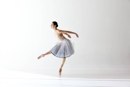 Solo performance. Ballerina dancing graceful movement in dress over white background. Art, motion, action, flexibility, inspiration concept. Beauty of contemporary dance