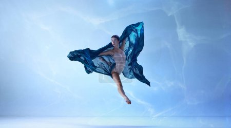 Photo for Flying with silk. Shot of jumping ballerina with stretched feet over blue background. Art, motion, action, flexibility, inspiration concept. Classic ballet. Beauty of contemporary dance - Royalty Free Image