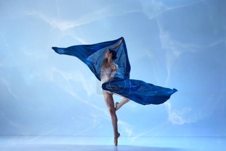Inspired beautiful ballerina dancing and looking away over blue background. Ballet with silk. Concept of classic ballet, inspiration, beauty, dance, creativity. Beauty of contemporary dance