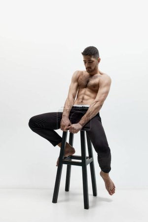 Photo for Shirtless. Portrait of attractive young muscular gay, man demonstrating his strength, power over white studio background. Concept of fashion, style, body aesthetics, beauty, mens health, ad - Royalty Free Image