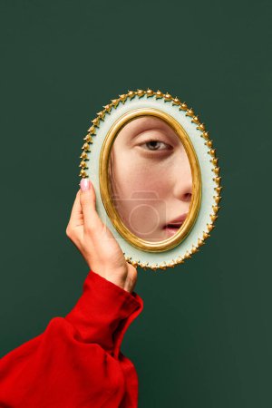 Photo for Female hand holding small mirror with reflection of sad womans face with natural make up over dark green background. Fashion, beauty, creativity, ad. Human emotions, expression concept - Royalty Free Image