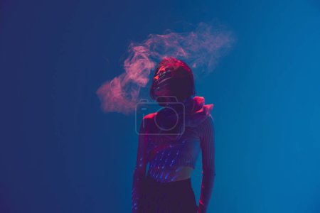 Photo for Nicotine addict. Portrait of beautiful sad woman, girl using vape, electronic cigarette over blue background in neon light. Concept of bad habits, emotions, digital art, fashion, cyberpunk, futurism - Royalty Free Image