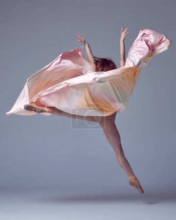 Ballet with silk. One charming professional ballerina wearing silk dress jumping up over grey studio background. Contemporary dance. Concept of classic ballet, inspiration, beauty, motion, creativity