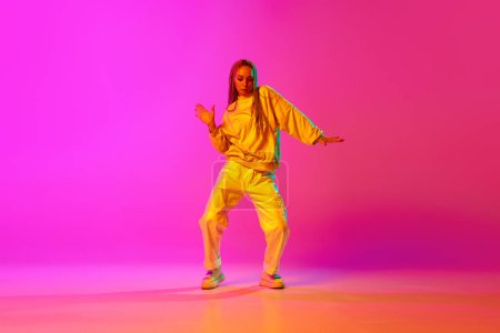 Portrait with one young beautiful girl, dancer with dreadlocks dancing over gradient pink background in neon light. Concept of contemporary dance style, motion, art, movement, inspiration, hobby, ad