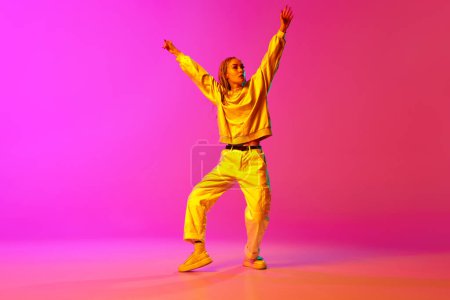 Portrait with one young girl, dancer with dreadlocks dancing with hands up over gradient pink background in neon light. Contemporary dance style, motion, art, movement, inspiration, hobby, ad concept