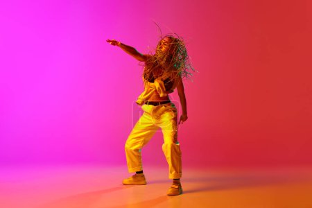 Un bailarín de hip-hop profesional que usa ropa de moda que se mueve con inspiración sobre el fondo rosa degradado en luz de neón. Concepto de estilo de danza contemporánea, movimiento, hobby, arte, anuncio