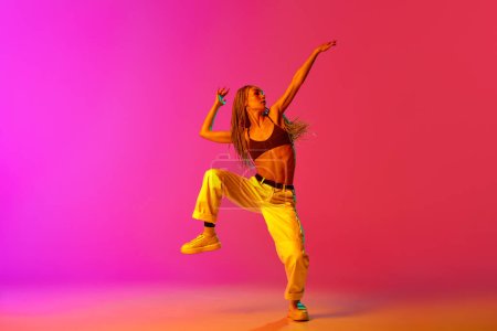Photo for Portrait of young stylish woman, hip-hop dancer training in casual clothes over gradient pink background in neon light. Youth culture, movement, street style, fashion, action, contemporary dance style - Royalty Free Image