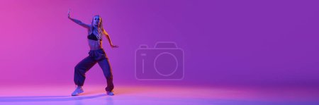 Portrait with young adorable girl dancing unusual movement over gradient purple background in neon light. Banner. Concept of contemporary dance style, motion, art, movement, inspiration, ad