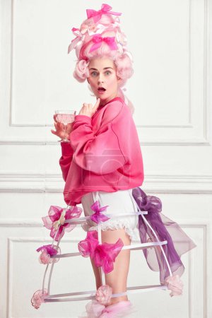 Photo for Royal party. Portrait of funny princess, queen wearing elegant pink clothes, and wig drinking cocktail over luxury interior background. Concept of comparison of eras, modernity and renaissance, beauty - Royalty Free Image