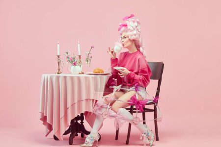 Photo for Royalty breakfast. Portrait of elegant princess, queen wearing pink clothes, and wig drinking coffee over pink background. Concept of comparison of eras, modernity and renaissance, beauty, history - Royalty Free Image