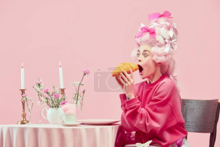 Photo for Portrait with surprised princess, queen wearing big wig and starting eat huge croissant on pink background with astonished face. Concept of food, diet, comparison of eras, modernity and renaissance - Royalty Free Image