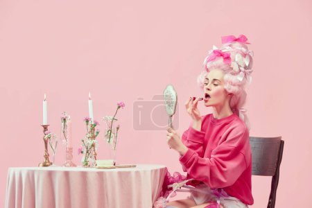 Photo for Beauty salon. Portrait with pretty princess, queen wearing big wig holding hand mirror and using lipstick on pink background. Concept of comparison of eras, modernity and renaissance, beauty, history - Royalty Free Image