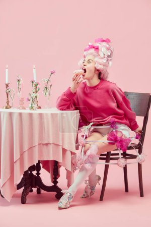 Photo for Sweet princess. Portrait hungry princess, queen wearing big pink wig eating donut with exciting face on pink studio background. Comparison of eras, modernity and renaissance, beauty, history concept - Royalty Free Image