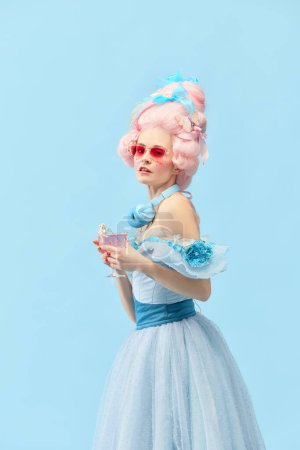 Photo for Royal family party. Portrait of young princess, queen wearing elegant dress, and pink wig drinking cocktail over blue studio background. Concept of comparison of eras, celebration, relaxing, party - Royalty Free Image