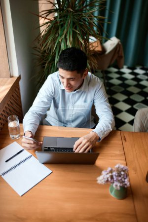 Handsome and successful businessman freelancer wearing classic clothes working with laptop and papers in cafe. Freelance work, startup, business people, remote job, career growth, ad concept