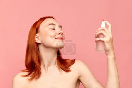 Photo for Portrait with redhead girl, model using moisturising spray on face with closed eyes over pink studio background. Facial cosmetics product, masks. Concept of natural beauty, skin care, cosmetology, ad - Royalty Free Image