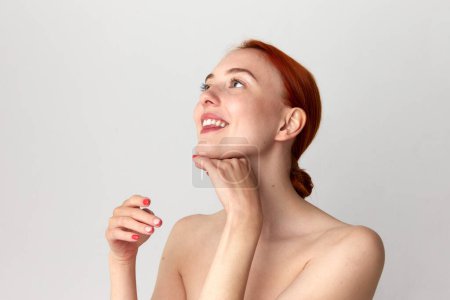 Photo for Close up shot of happy, adorable girl with perfect skin and red hair doing neck massage over white studio background. Beauty, spa, cosmetology, skin care, emotion concept. Model with well-kept skin - Royalty Free Image
