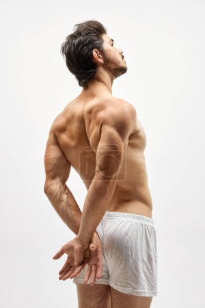 Muscled model. Portrait of handsome young dark-haired man posing isolated over studio background. Male natural beauty. Concept of mens health, posing, beauty, body and skin care. Fashionable look
