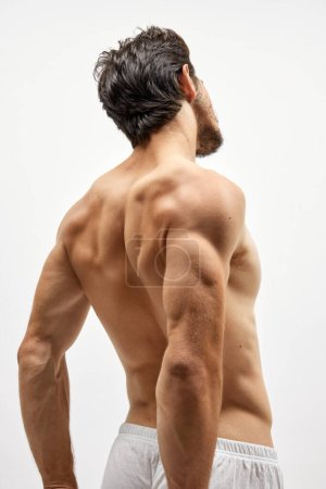 Foto de Fuerza, poder y belleza. Vista posterior de un hombre joven musculado fuerte posando en topless sobre fondo blanco. Concepto de belleza, moda, deporte, fitness y cuidado corporal - Imagen libre de derechos